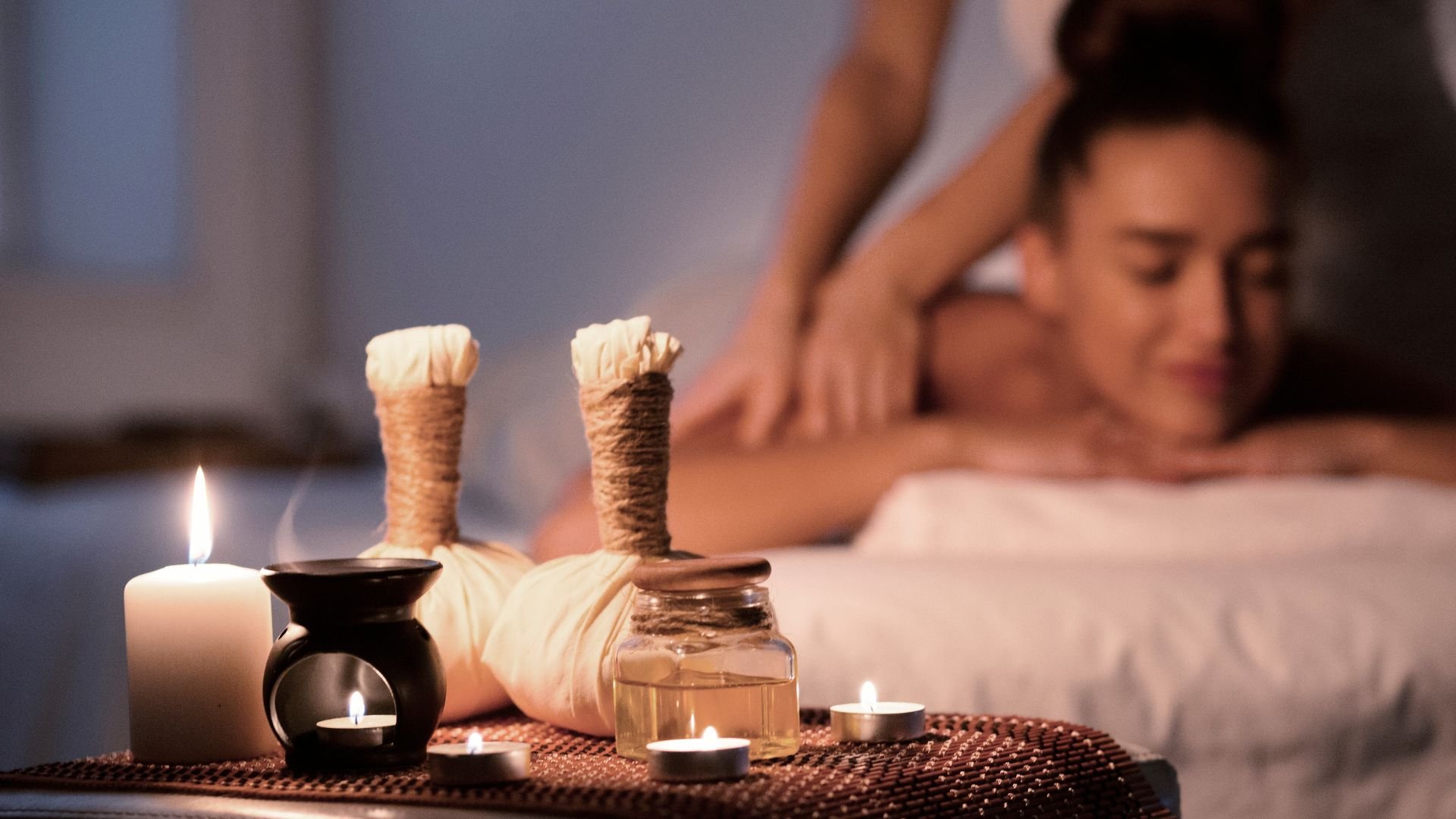 Spa massage setting with herbal compress, candles, and massage oil