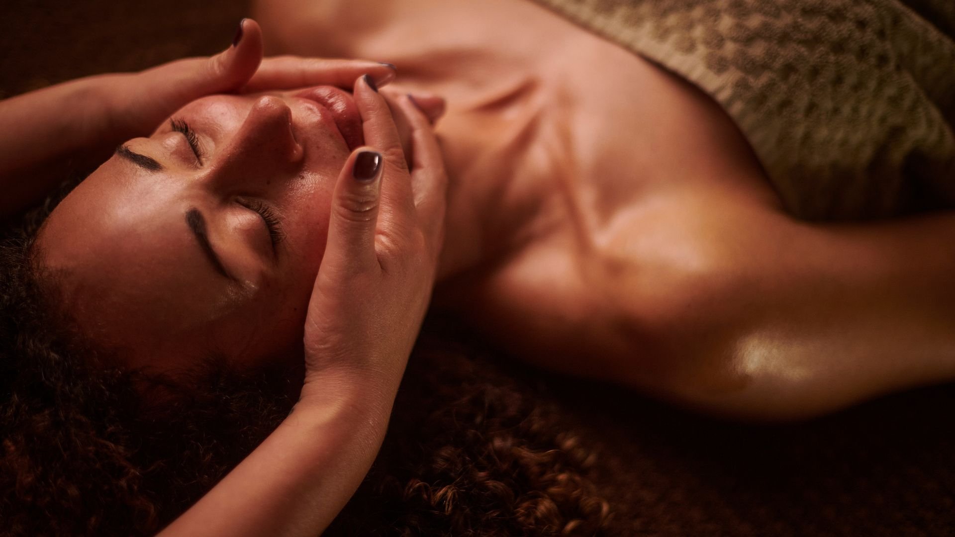 Person receiving facial massage with eyes closed, warm lighting