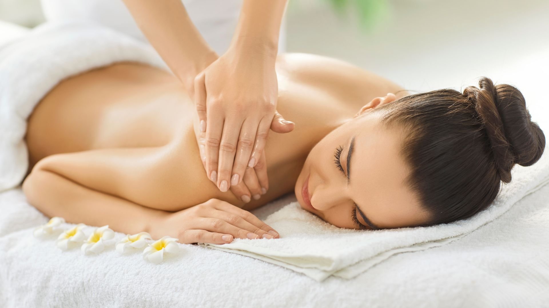Relaxed person receiving massage on white towel with flower petals